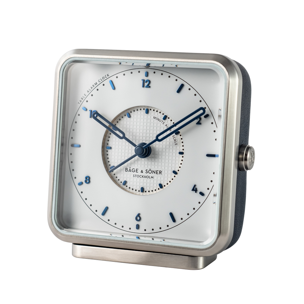 Elegant 'Afternoon Delight' alarm clock showcasing a white dial with blued numbers and Tappisserie design, encased in stainless steel