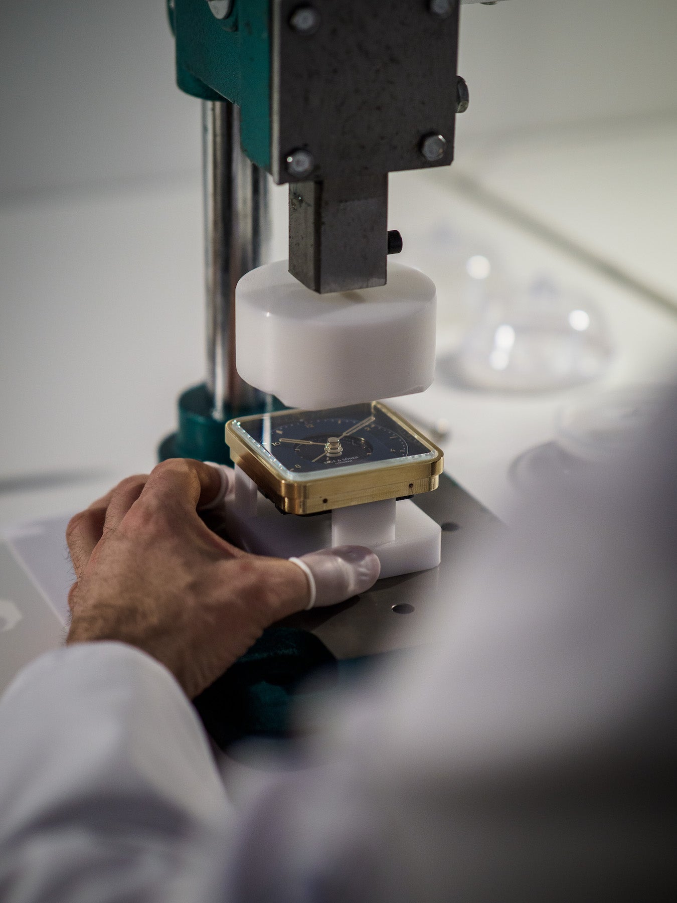 Craftsman at work in the workshop, meticulously assembling the 'Everglow' alarm clock with its sunray-accented white dial and brushed gold-plated edges, against the backdrop of tools and materials, highlighting the hands-on quality and care in creating the opulent piece with its vibrant orange leather detail