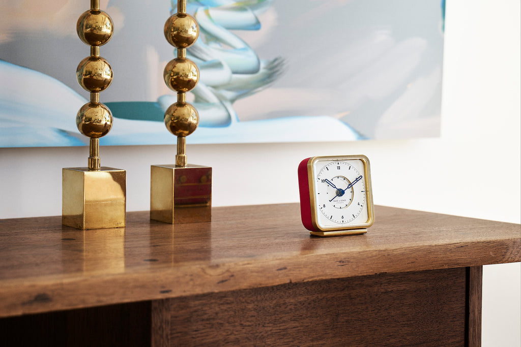 French Kiss' alarm clock on a nightstand, white dial contrasting beautifully with red leather