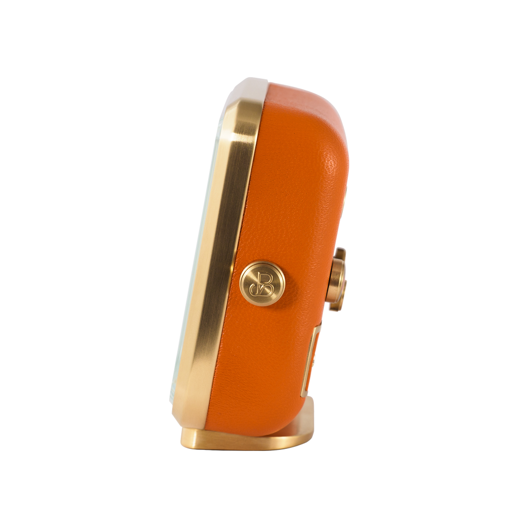 Gold-plated edge and vibrant orange leather highlight the side view of 'Everglow' alarm clock